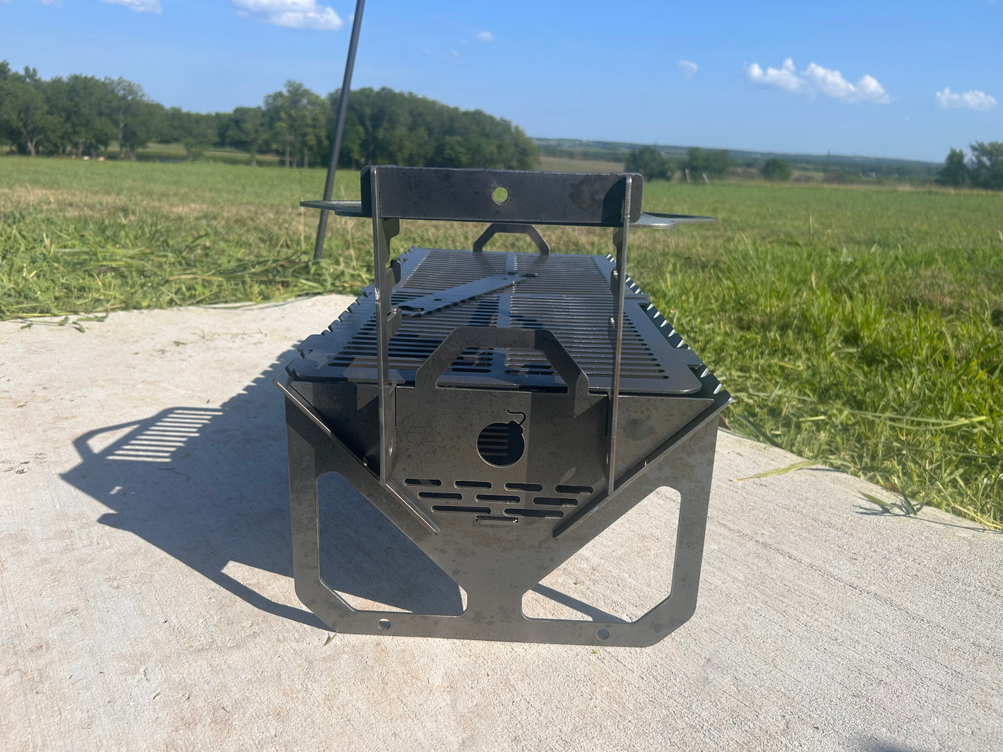 Metal grill on a concrete surface with a grassy field and trees in the background