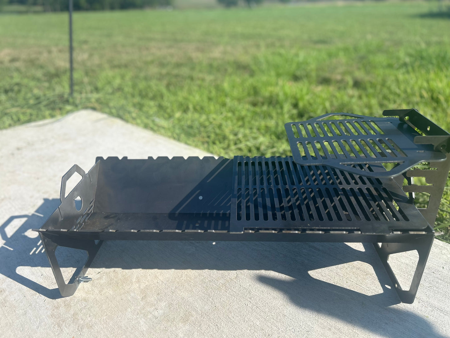 Black metal grill on a concrete surface with grass in the background