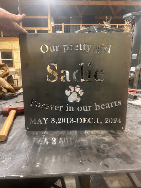 Metal plaque with engraved text and a paw print on a workshop background